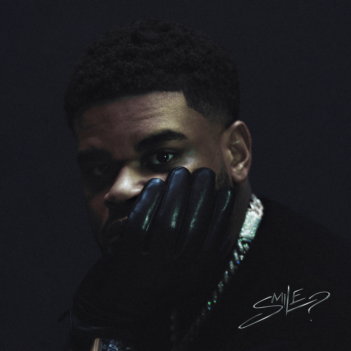 Close-up of a man in leather gloves, dark background, album cover.