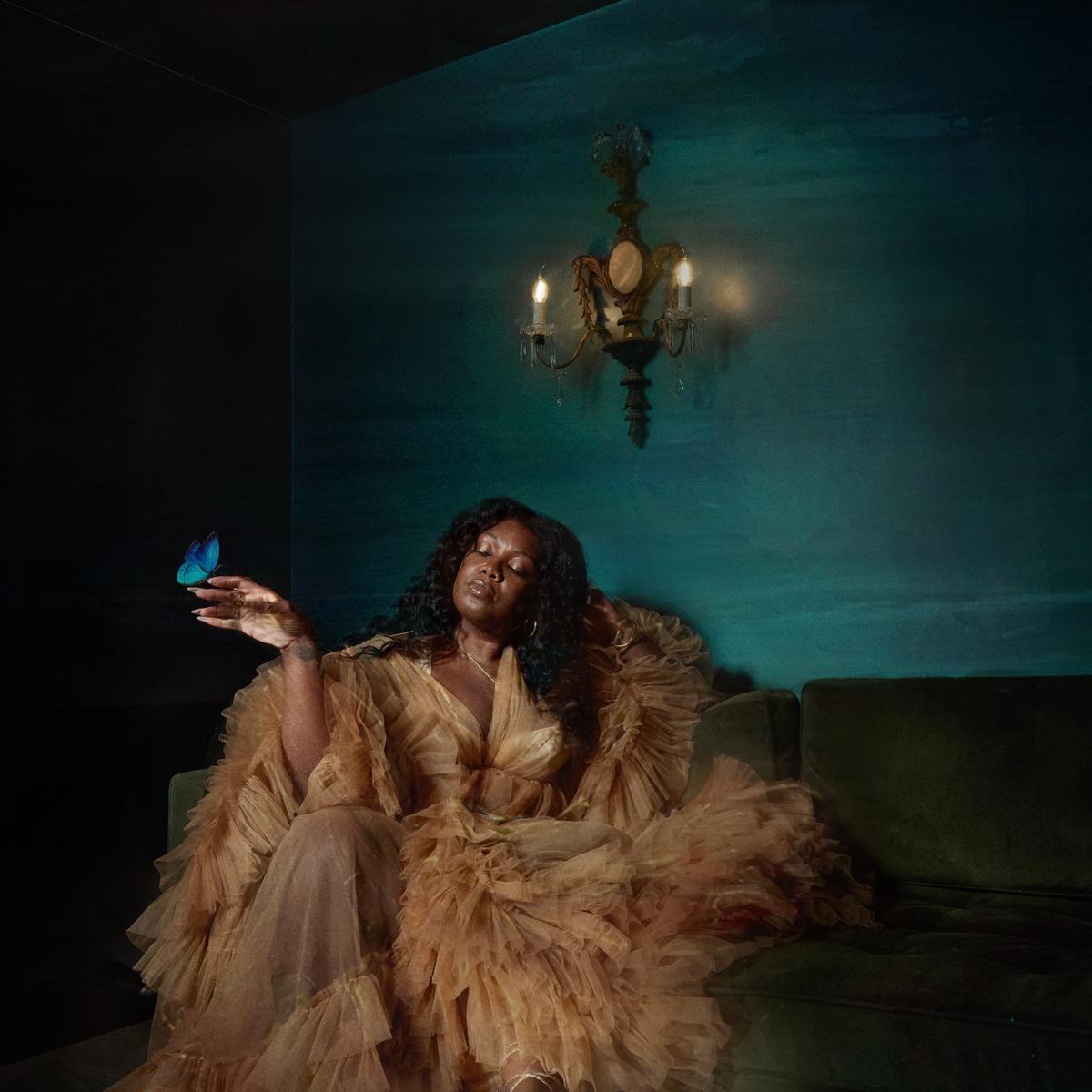 Woman in a ruffled dress sits beneath a candle sconce and butterfly.