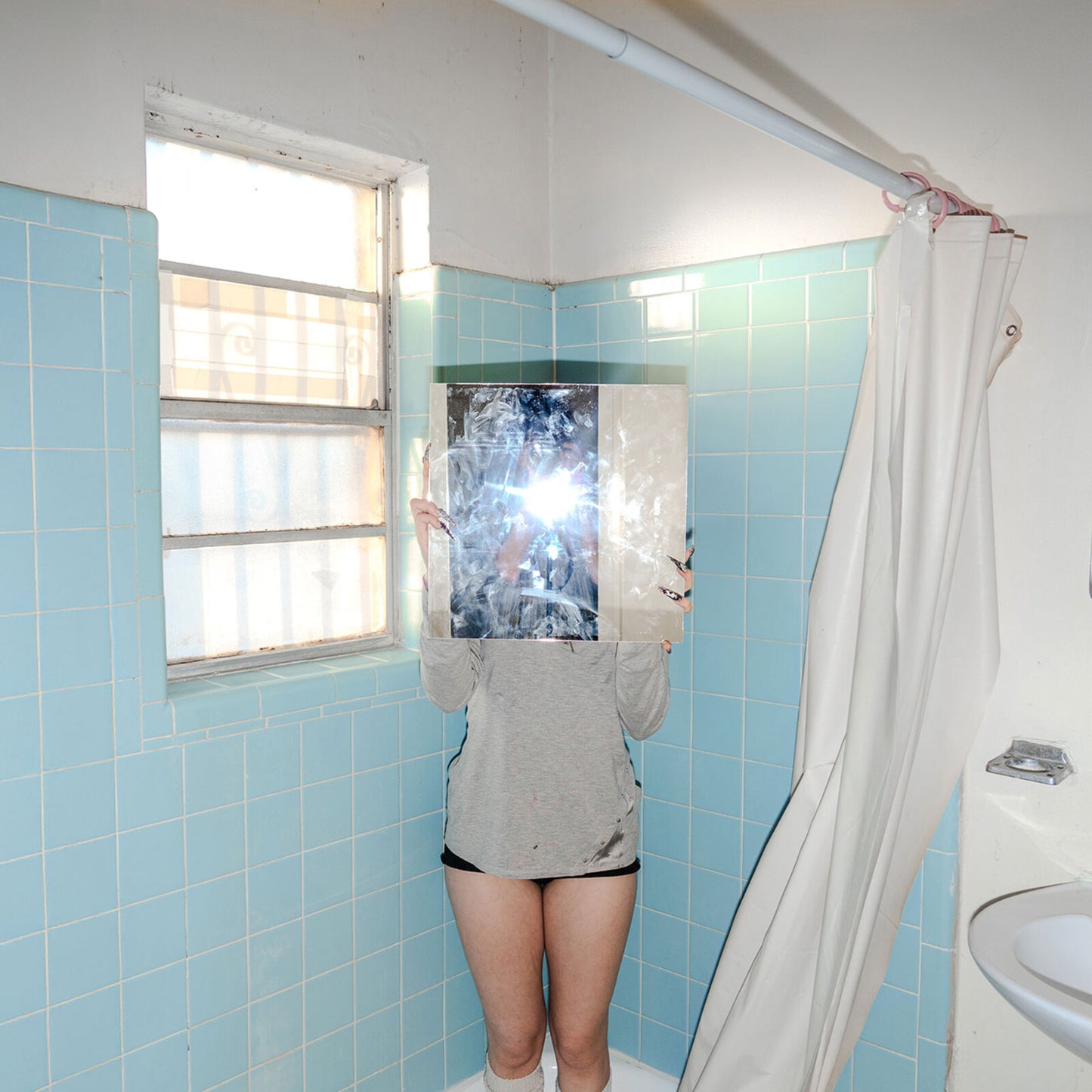 Person holding a CD case in front of their face in a bathroom.