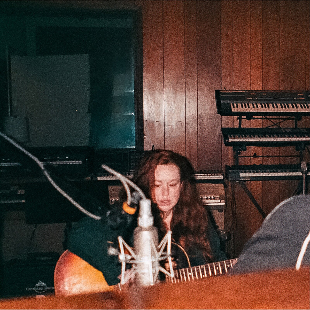 Woman with long hair singing into a microphone with a guitar.