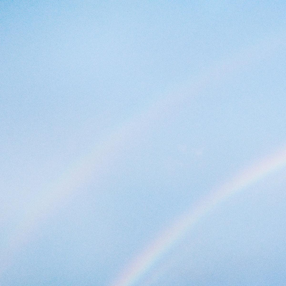 Pale blue sky with a faint, curved rainbow in the lower right.