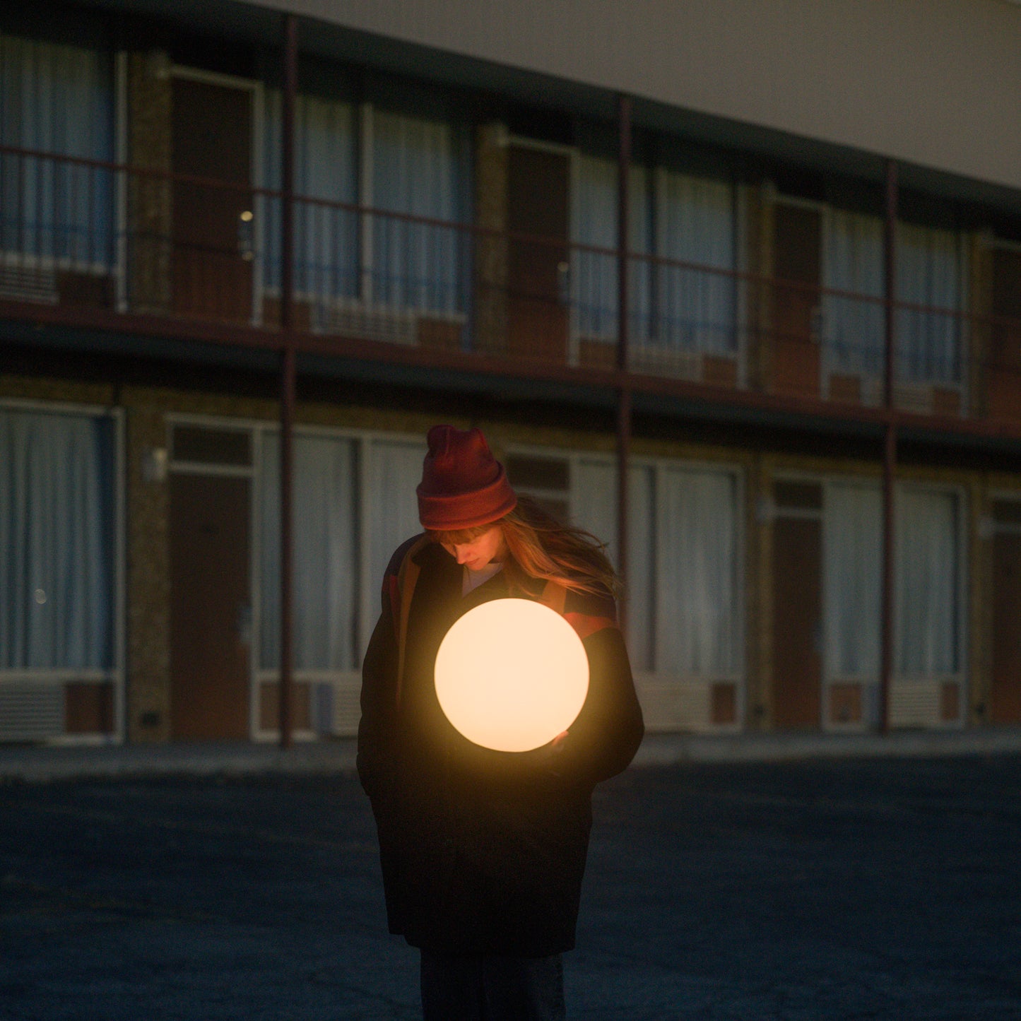 Person with illuminated orb stands before a multi-story motel.
