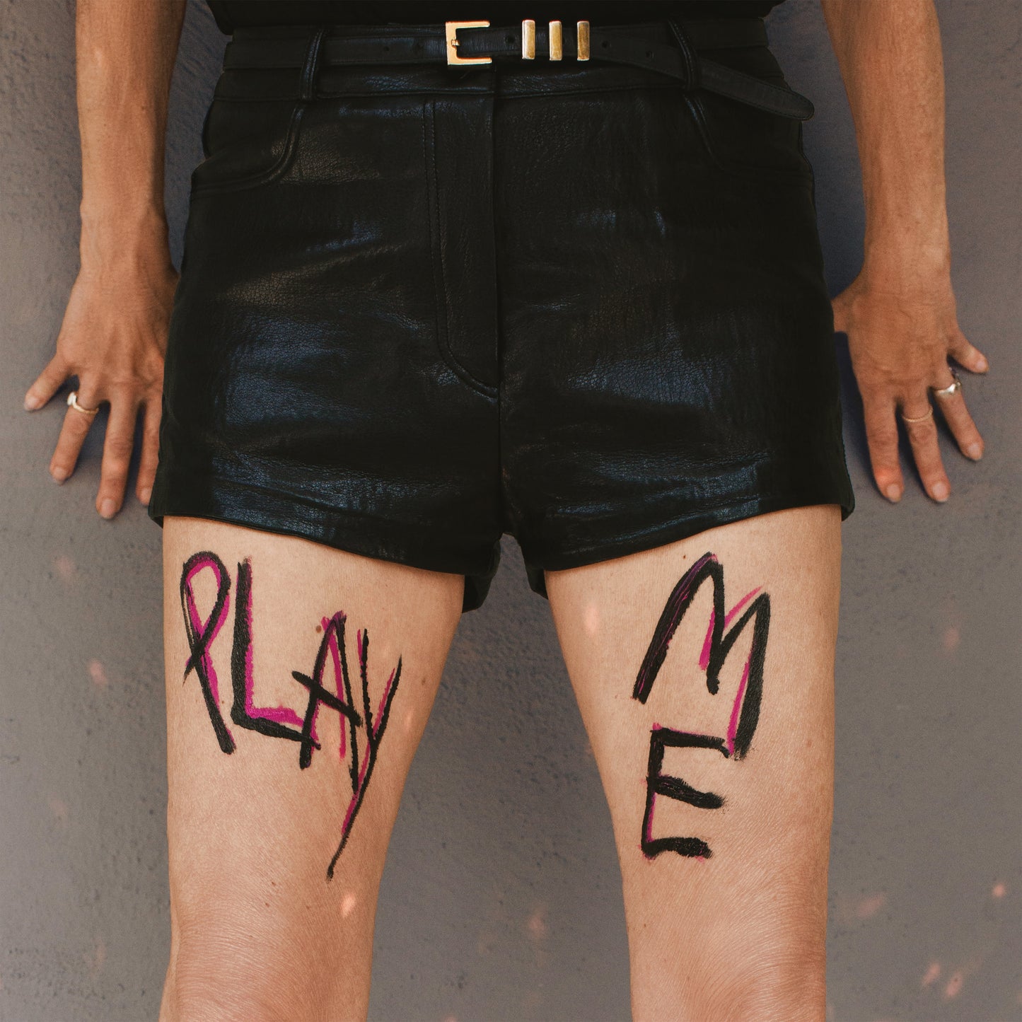 Vinyl record cover with legs featuring handwritten "PLAY ME" text.