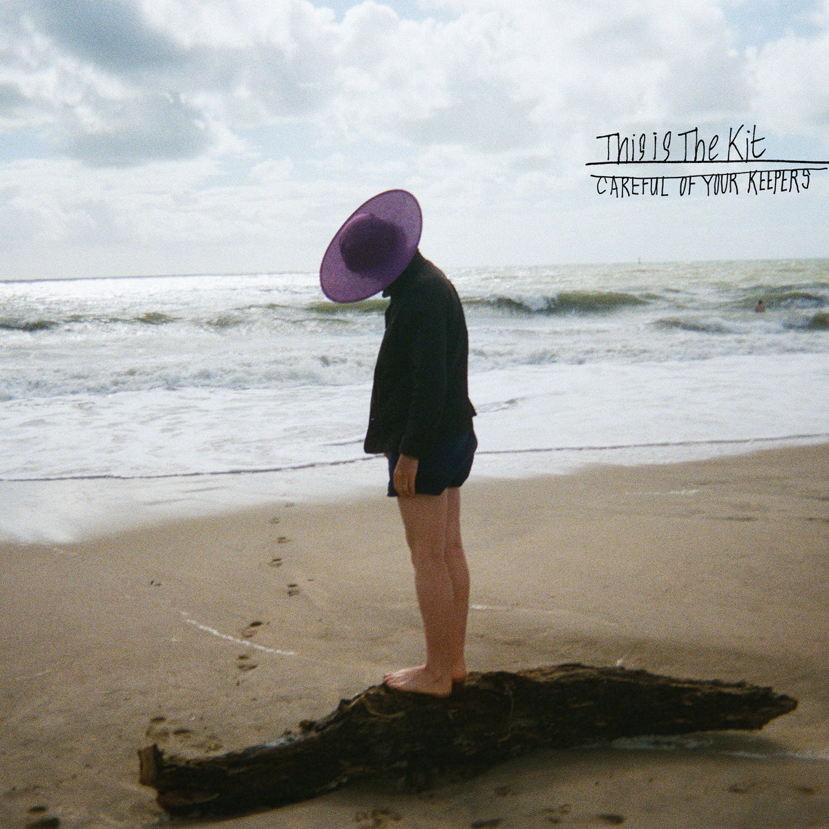 Album cover: person in hat standing on beach, looking at sea.