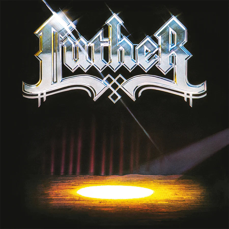 Shiny metallic Luther logo above a stage with a bright spotlight on dark floor.