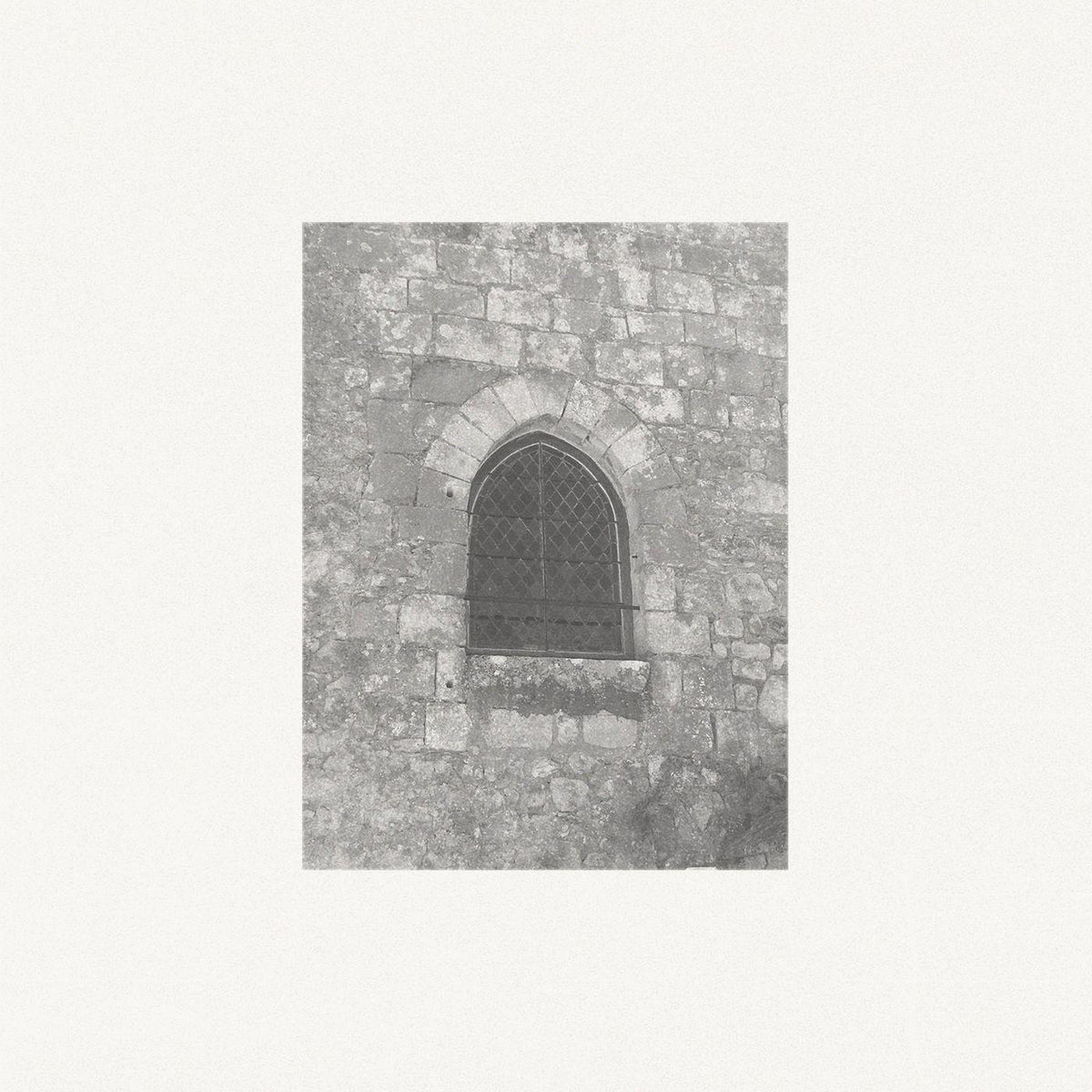 Black and white photo of a stone wall with a small arched window.