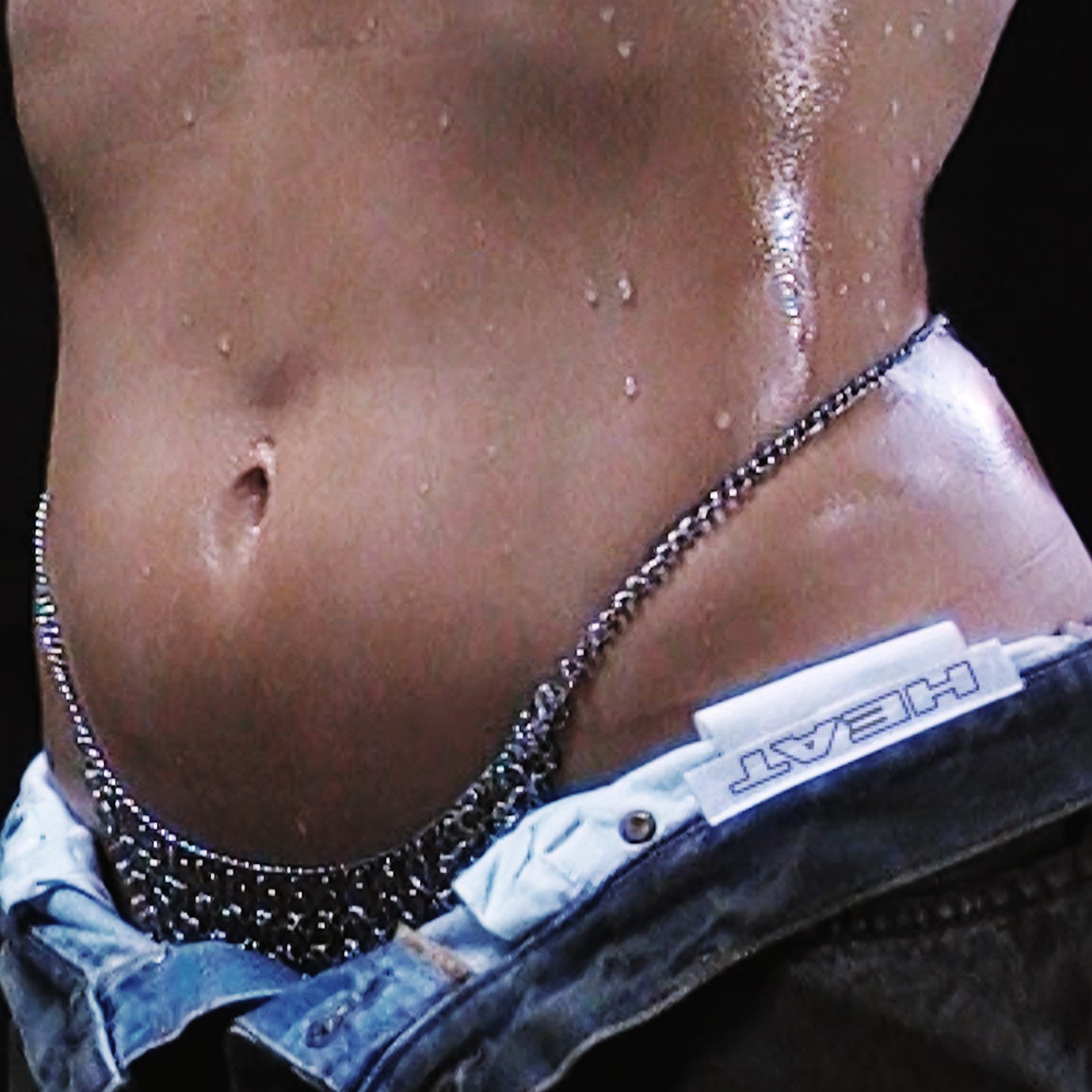 Close-up of a wet torso with a silver chain and jeans labeled "HEAT".