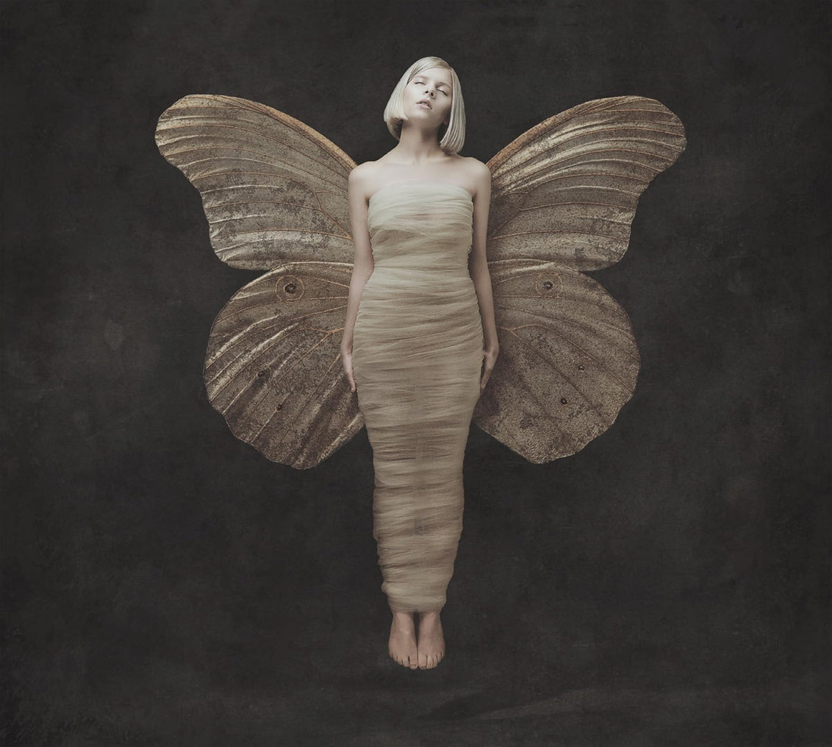Woman with large moth wings, standing against a dark background.