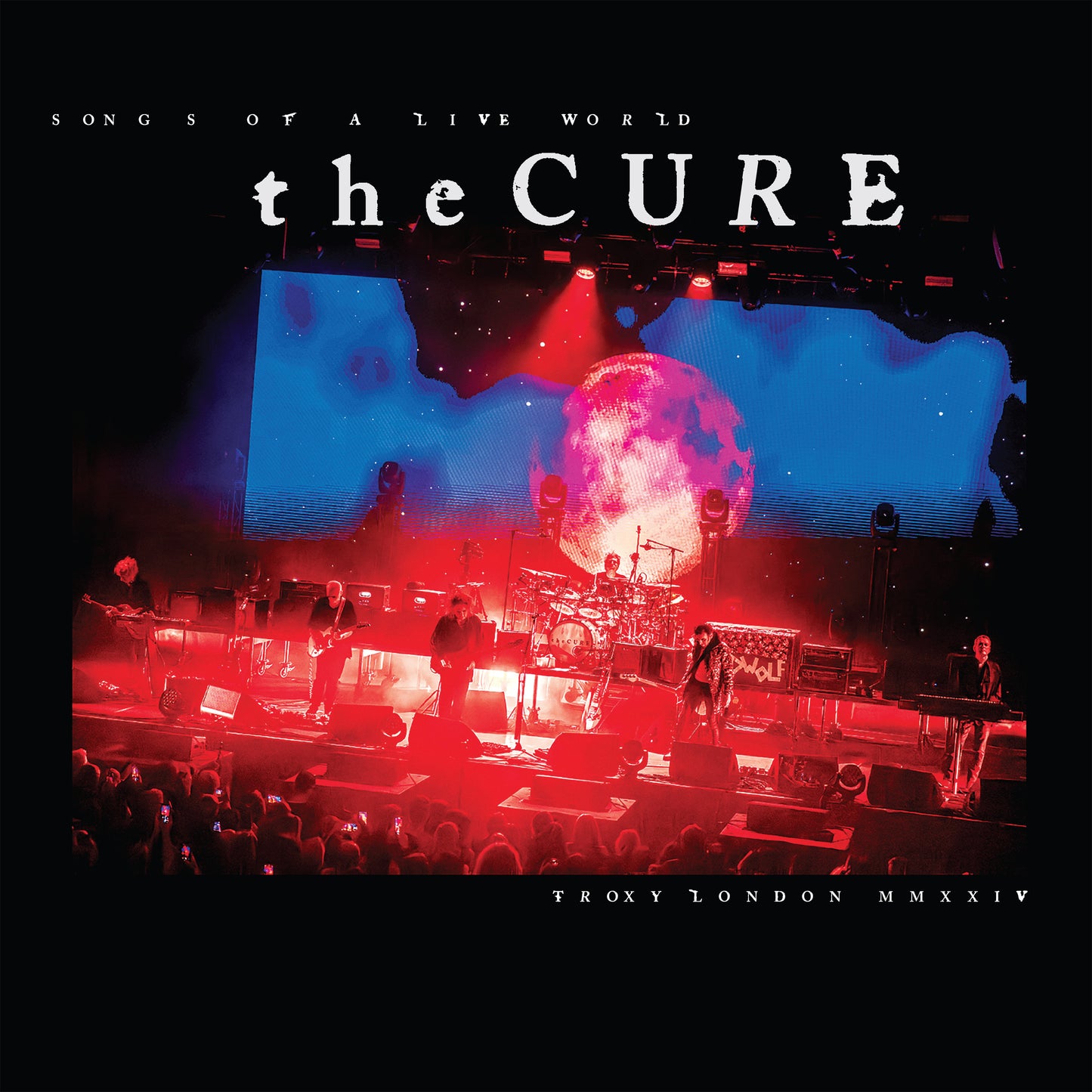 The Cure performing live on stage with red and blue lighting.