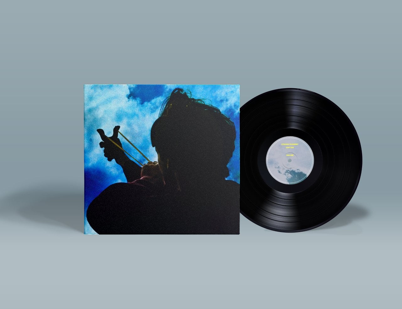 Vinyl record and album cover with silhouette against a blue sky.