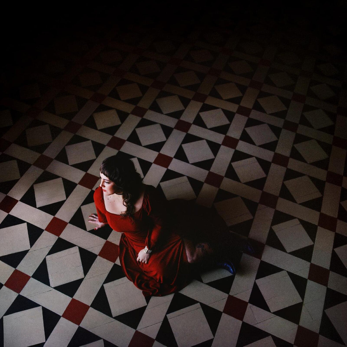 Woman in red sits on patterned tile floor, viewed from above.