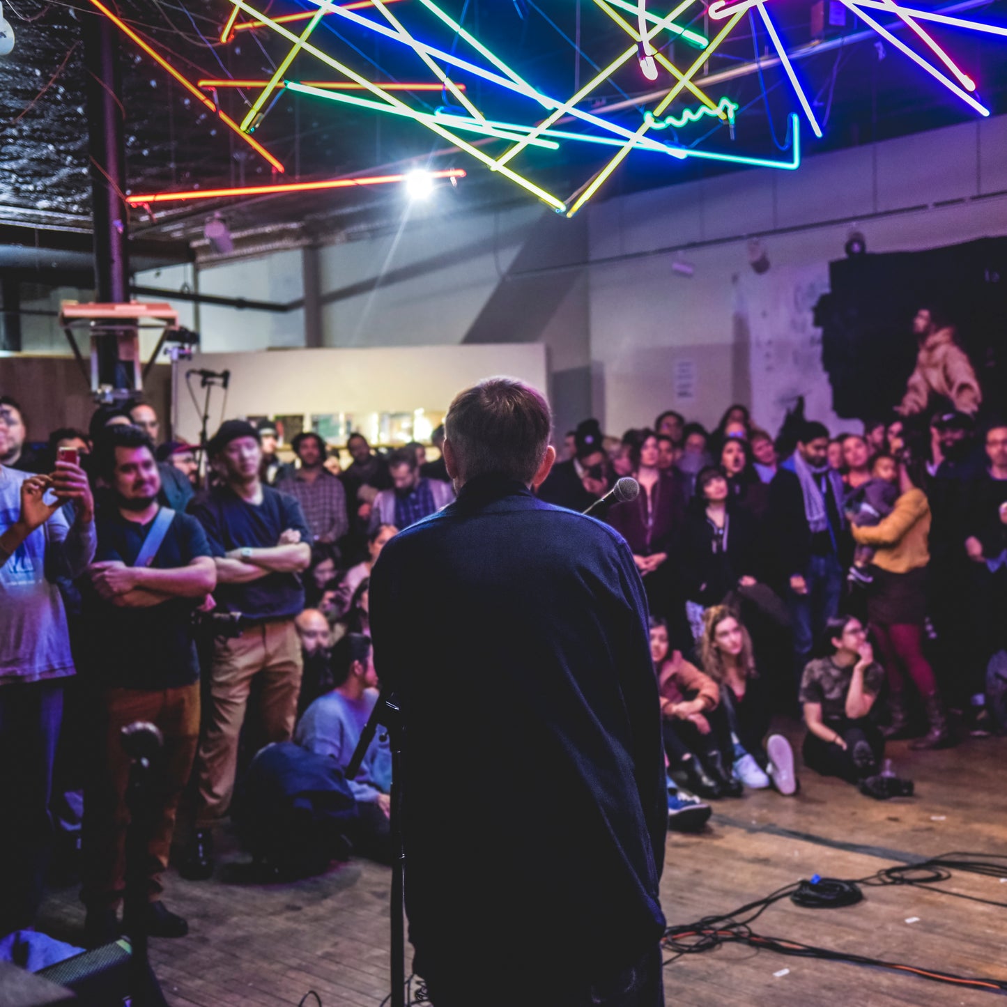 Man speaking into a microphone before a seated, diverse crowd.
