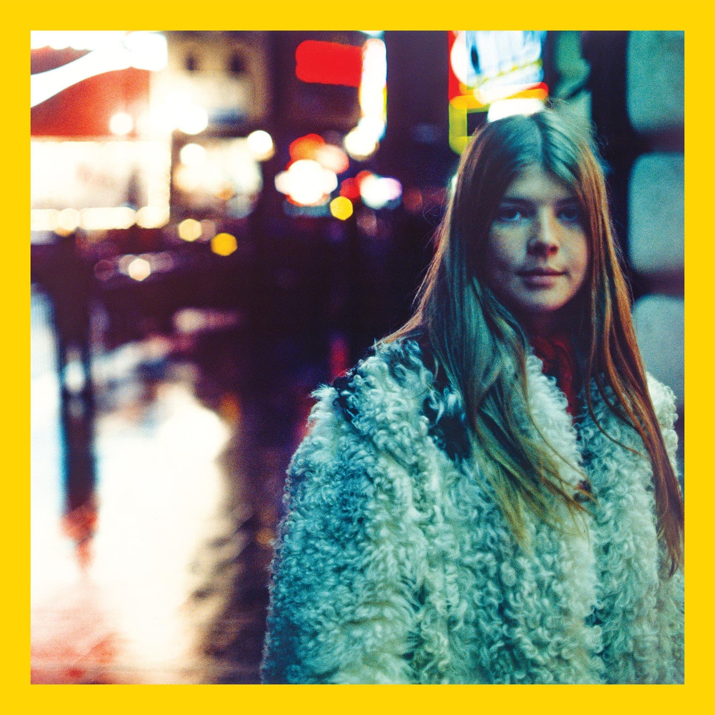 Woman with long hair in a fluffy coat, city lights blurred.