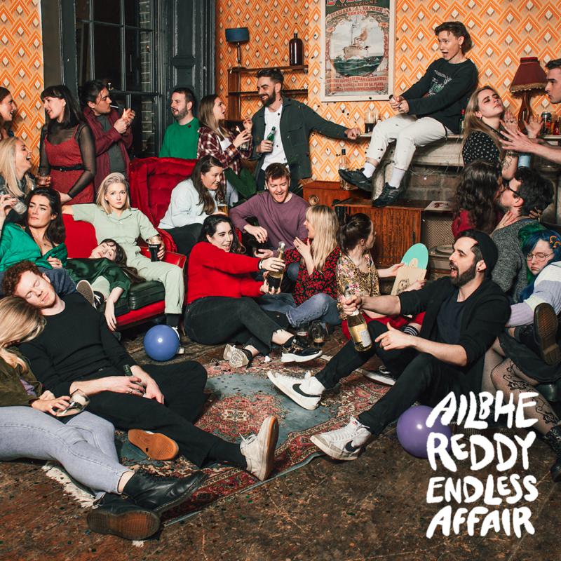 Group of people casually gathered in a patterned room, album cover.