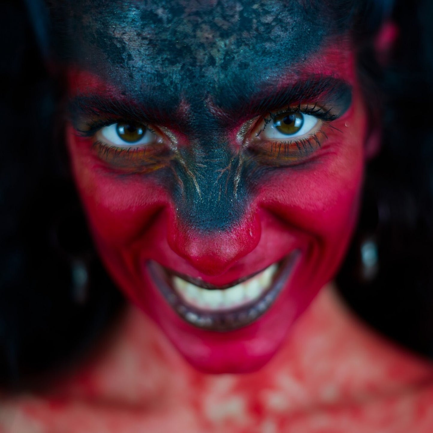 Close-up of a person with red and black face paint, smiling intensely.