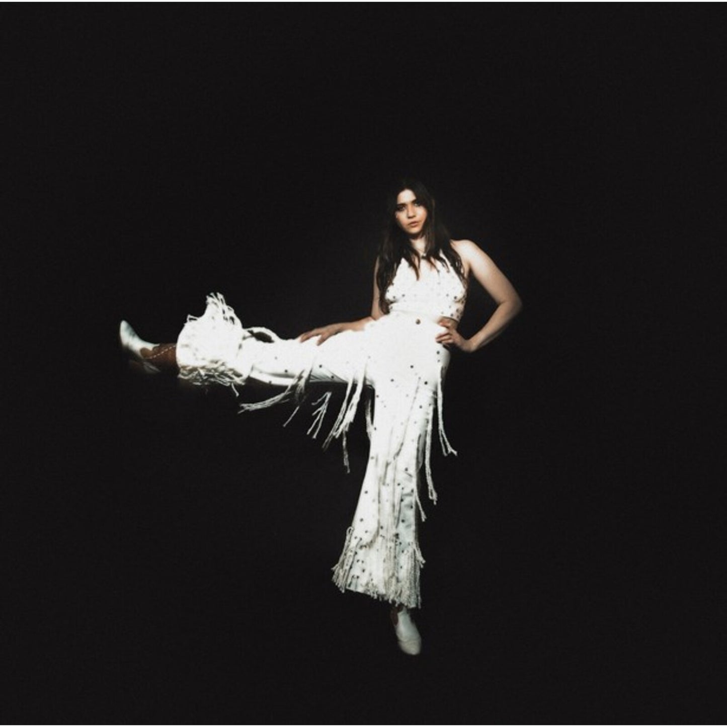 Woman in white fringed outfit posing against a black background.