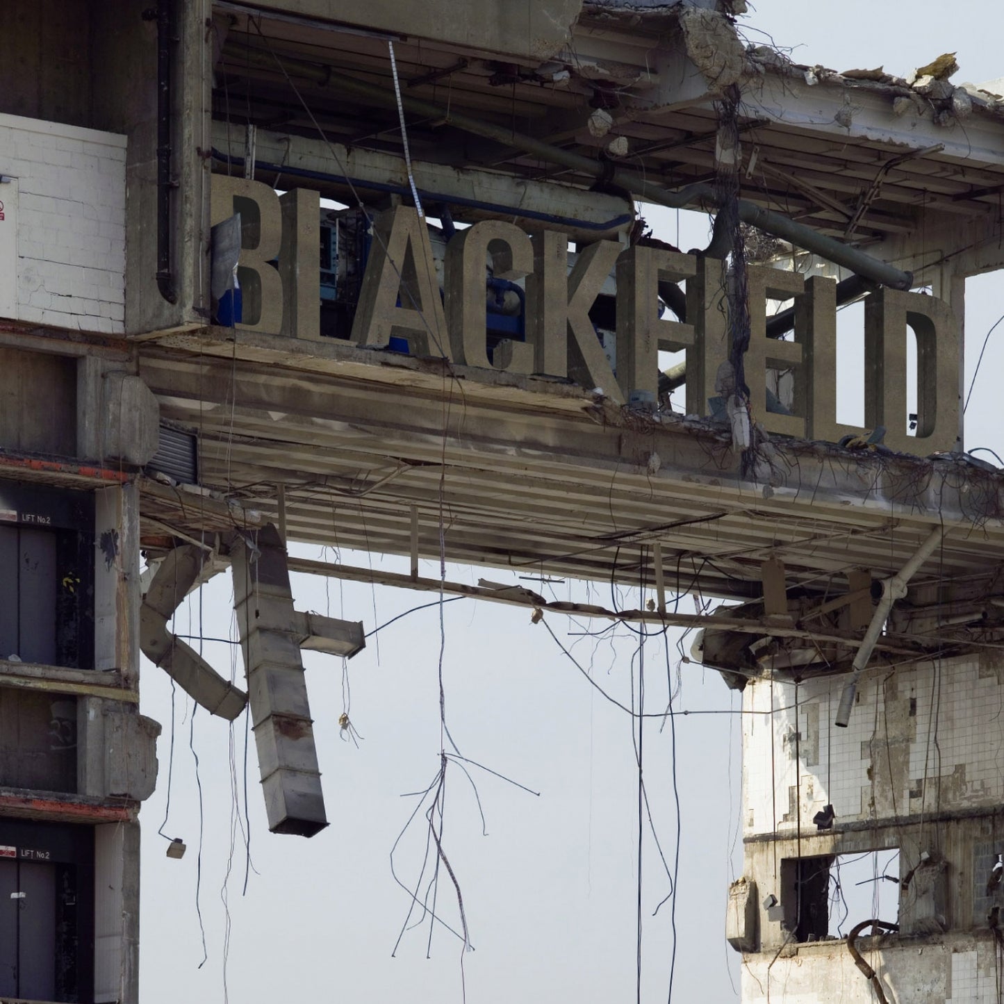 Large letters spelling Blackfield on a ruined, decaying concrete building structure with hanging wires.