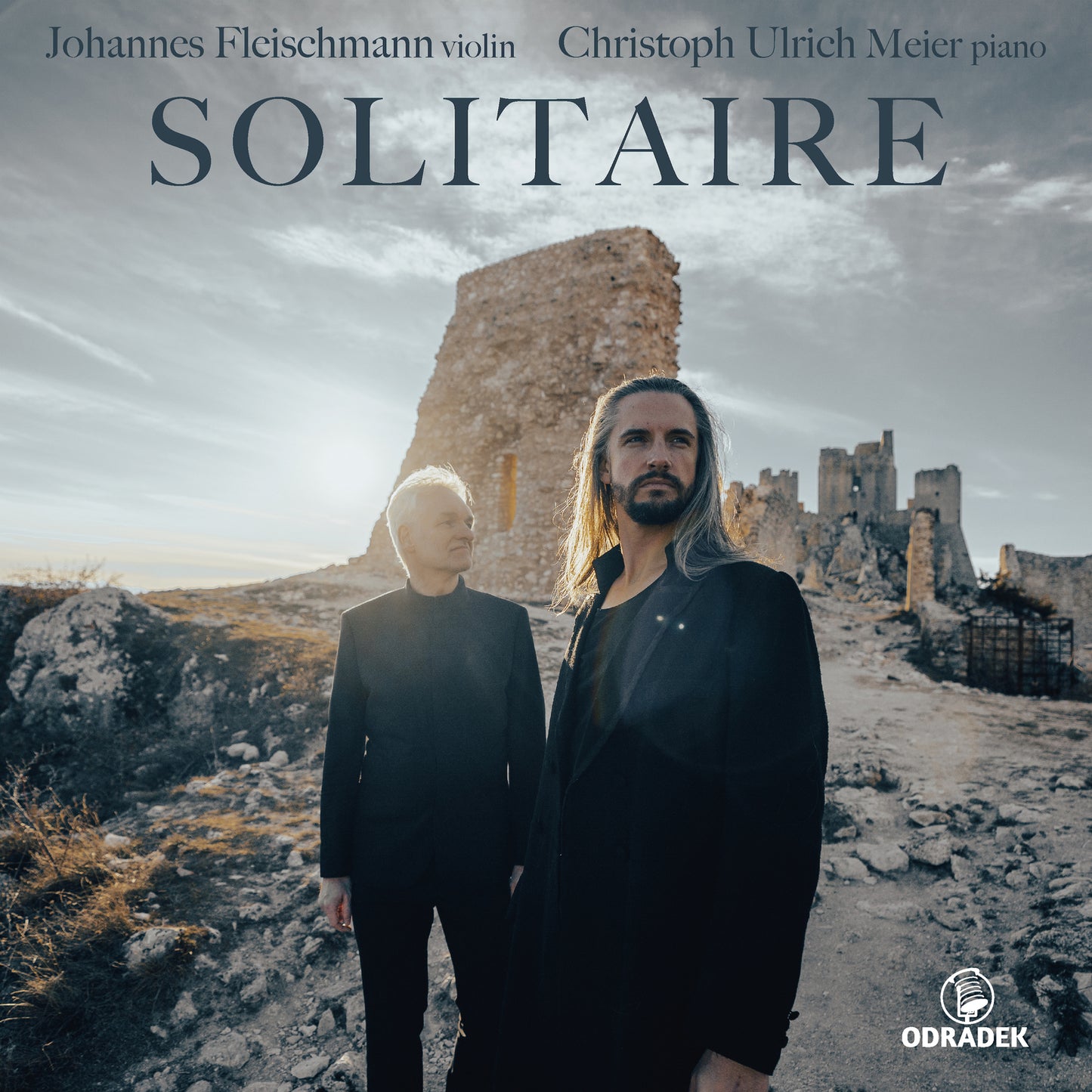 CD cover: two men stand before a ruined castle in sunlight.