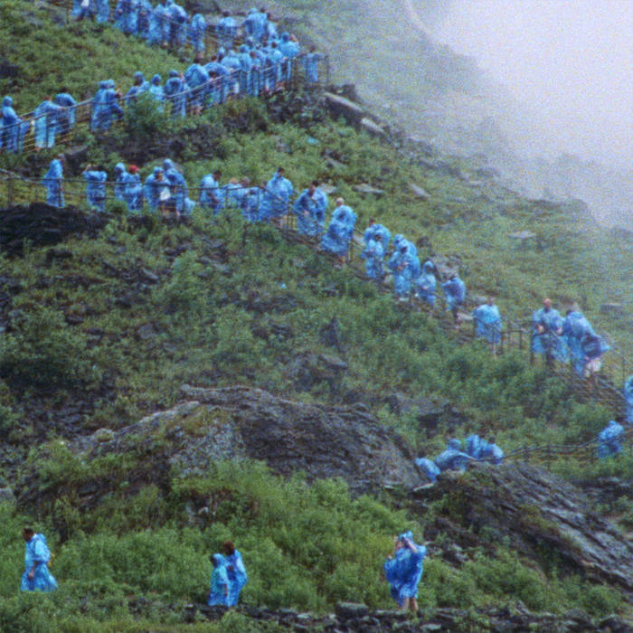 Large group of people in blue raincoats walking up a green hillside.