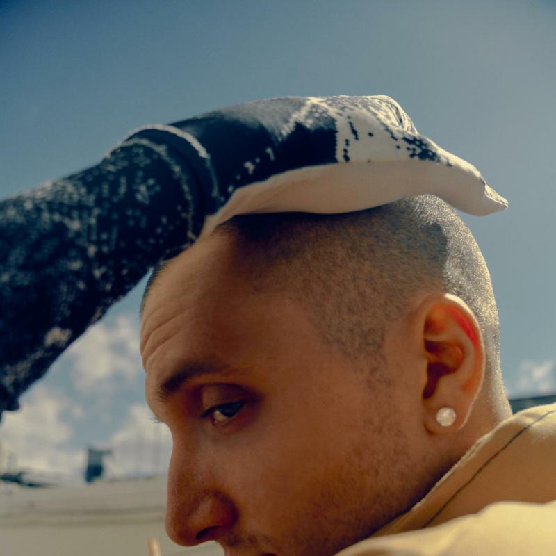 A gloved hand rests on the head of a person against a blue sky.
