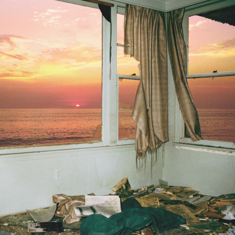 Sunset over the ocean viewed from a messy room with curtains.