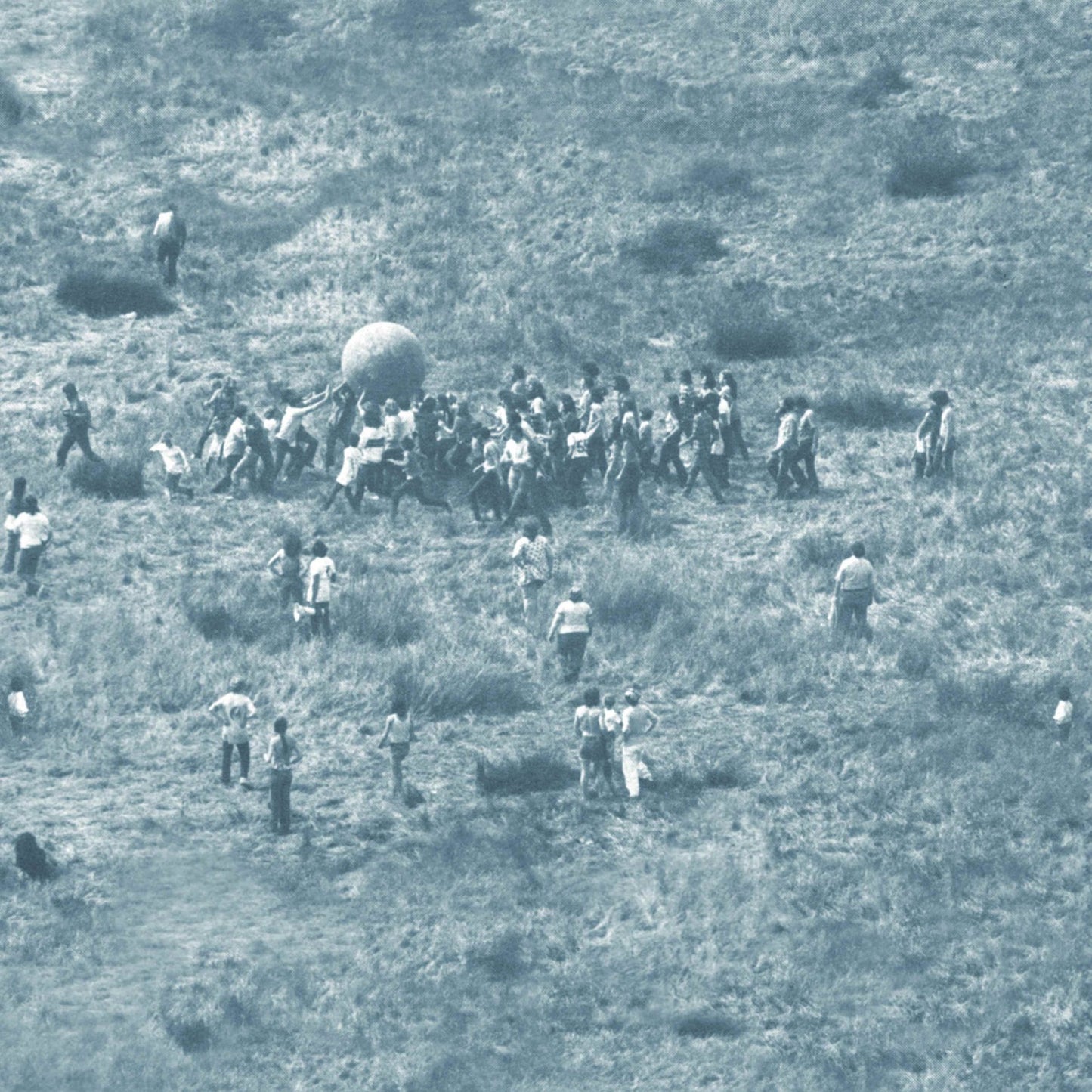 Group of people pushing a large ball across a grassy field.