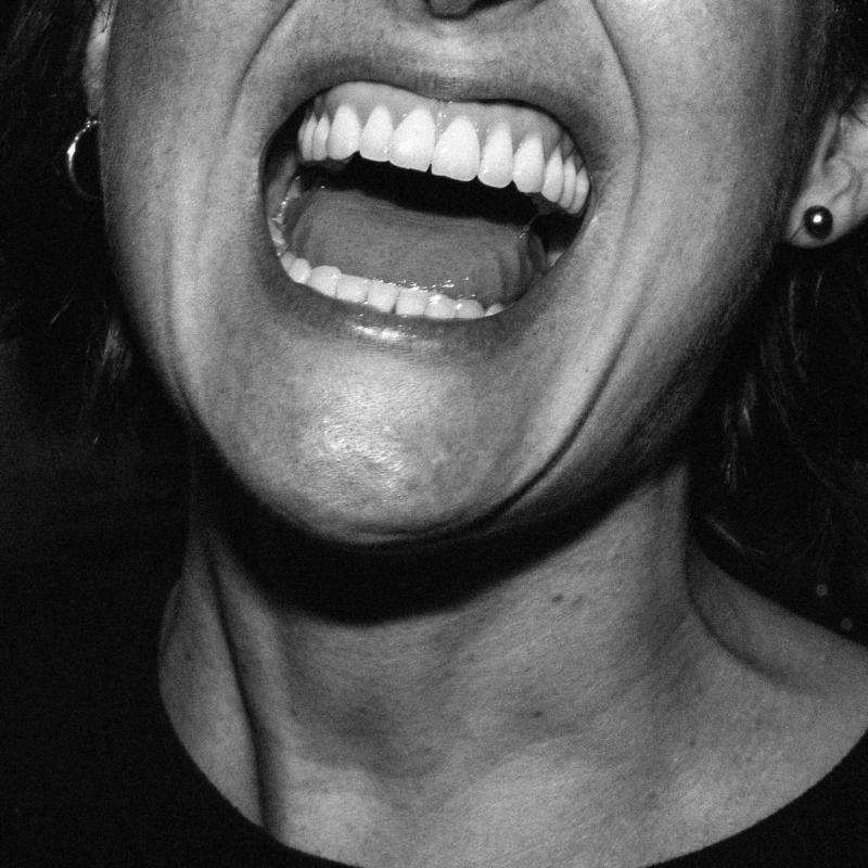 Black and white close-up of a person with an open mouth, yelling.