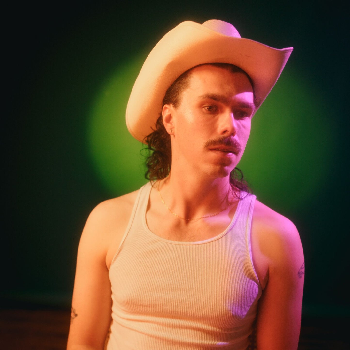 Man with curly hair wearing a white cowboy hat and tank top.