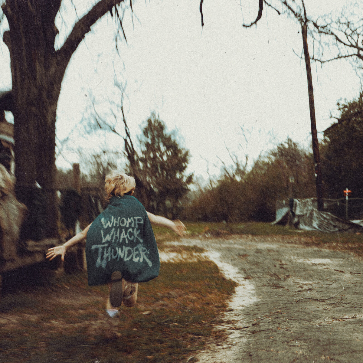 Child running on a rural road, wearing a shirt with text.