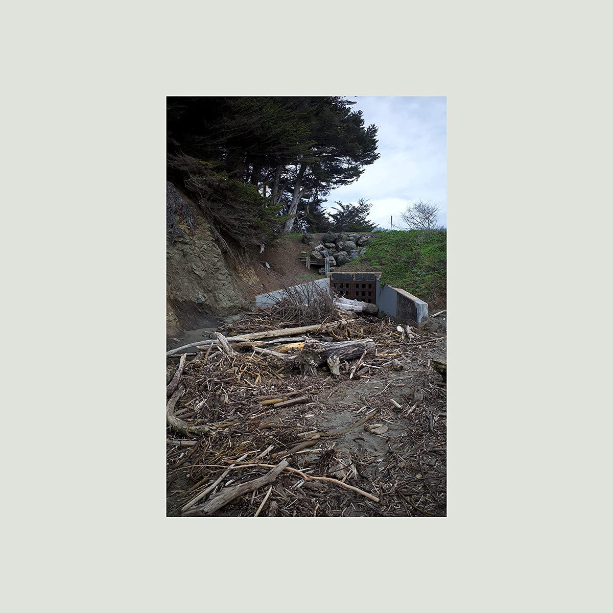 Overcast landscape with debris, a concrete structure, and trees.