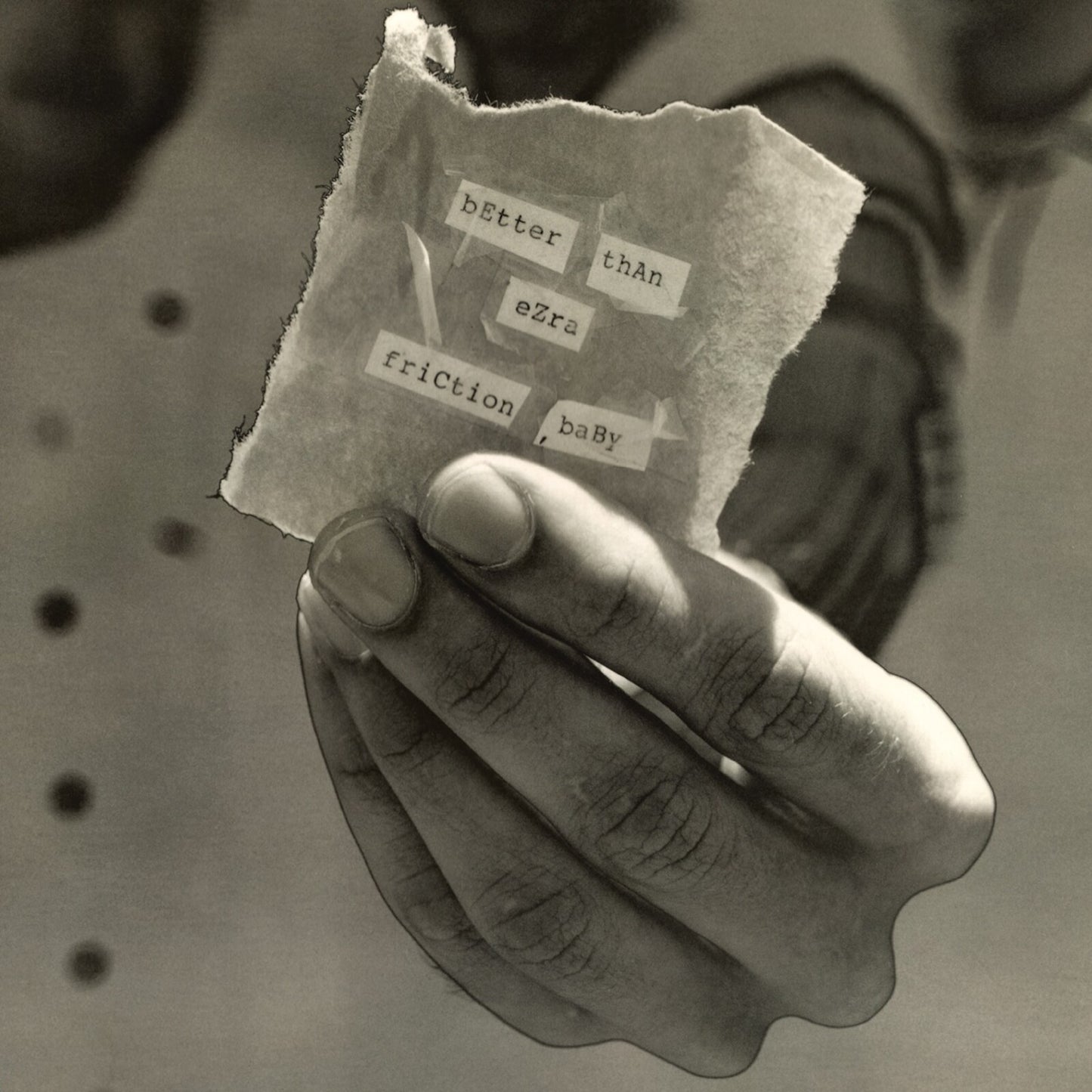 Hand holding torn paper with typed text: "Better Than Ezra - Friction Baby".