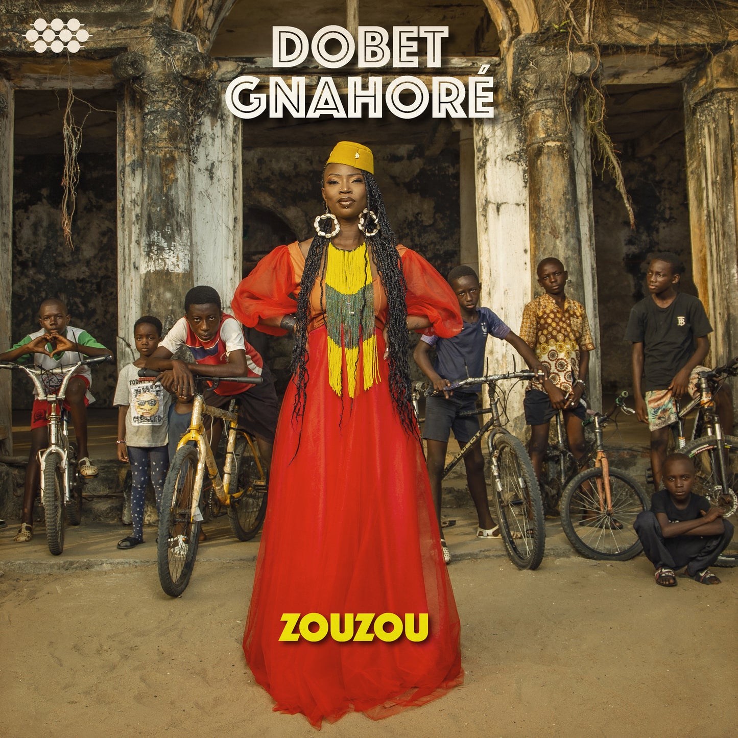 Dobet Gnahore in red dress with children and bicycles outdoors.