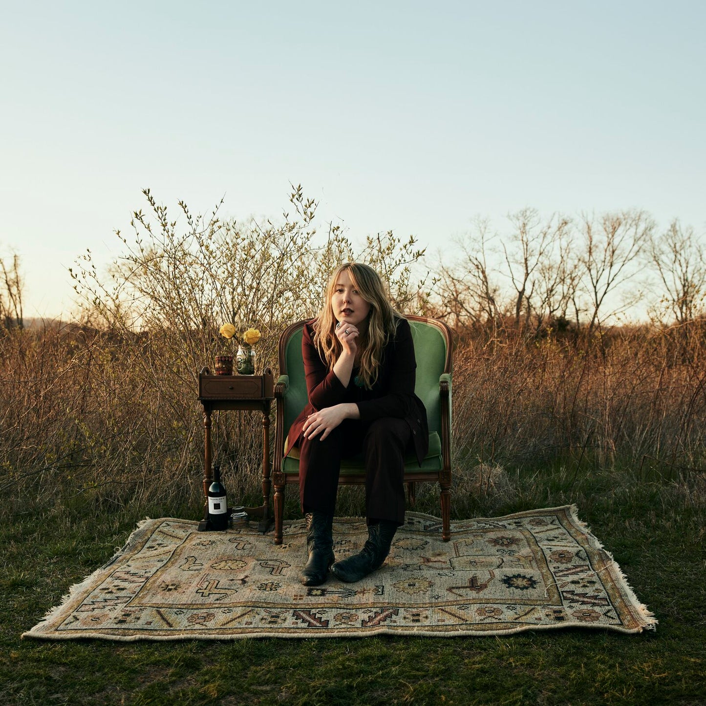 Woman sitting in green chair on rug in a field.