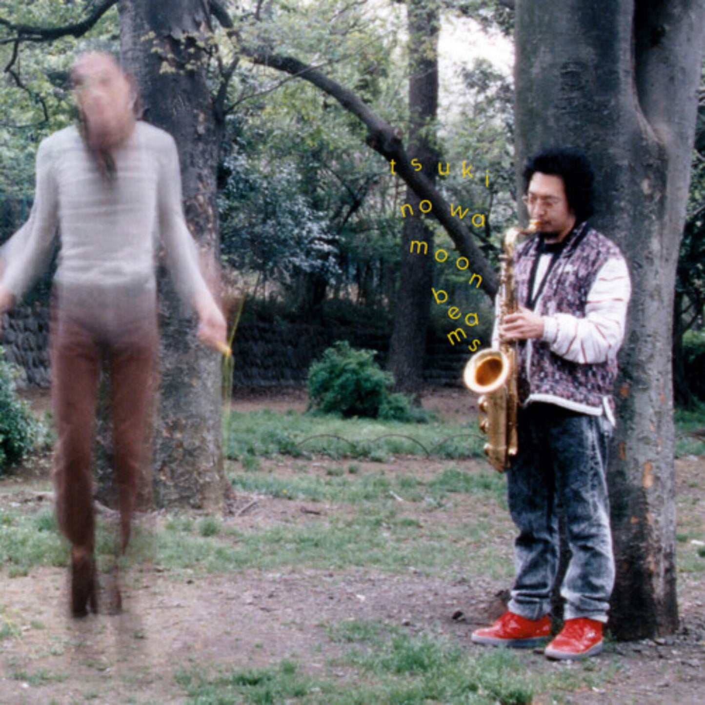 Man with saxophone stands near a blurred figure in a park.