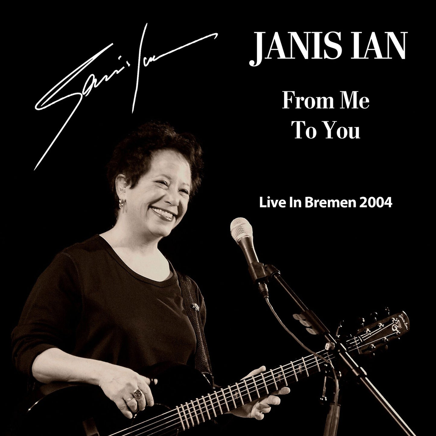 Janis Ian smiling, holding a guitar and microphone on a black background.