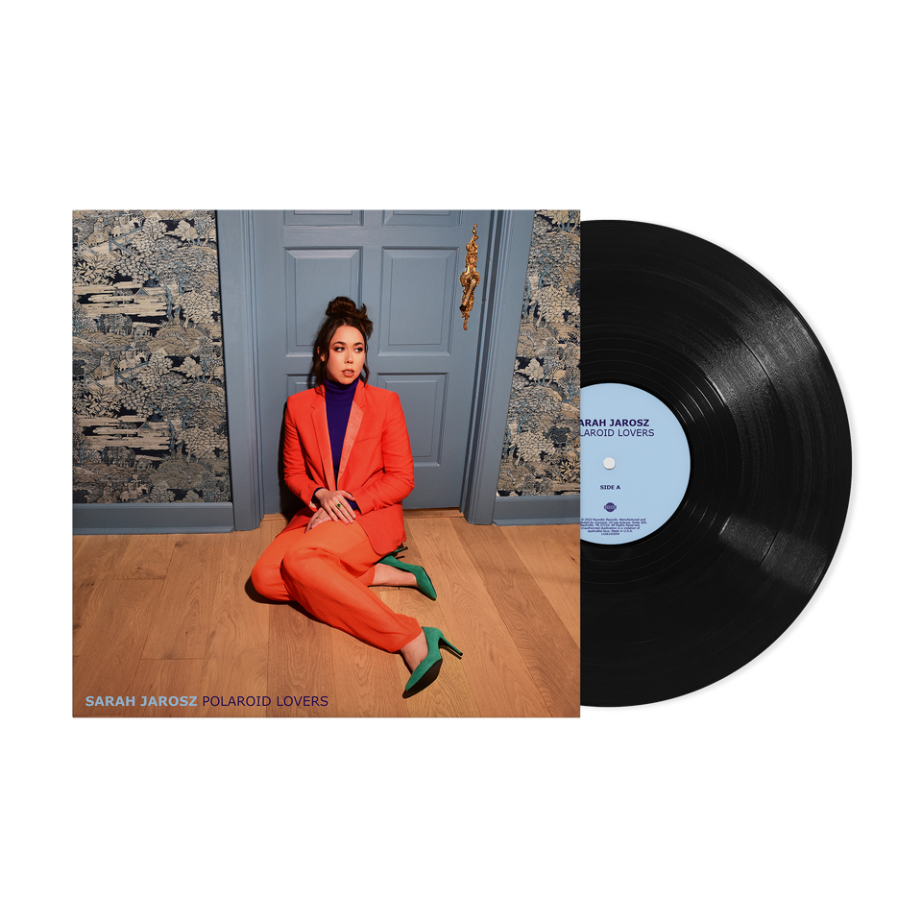 Woman in orange suit sitting on floor beside vinyl record and album cover.