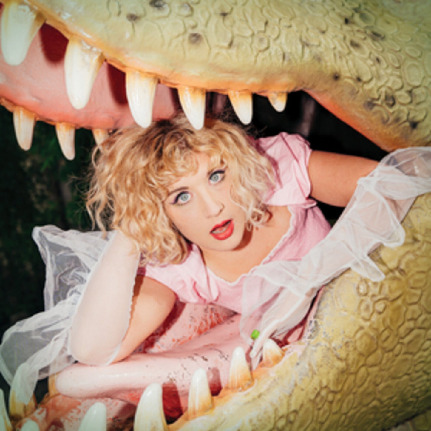Woman with blonde curls inside the open mouth of a dinosaur.