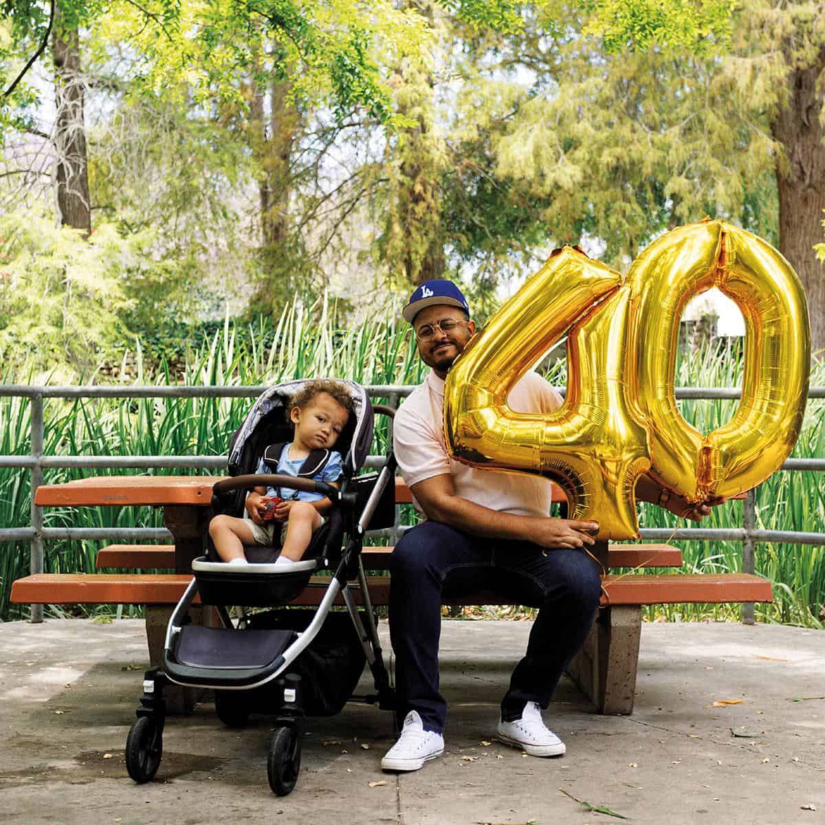 Man with baby and large gold "40" balloons outdoors.