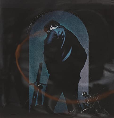 Man in dark clothing standing in front of blue archway with sword and skeleton.