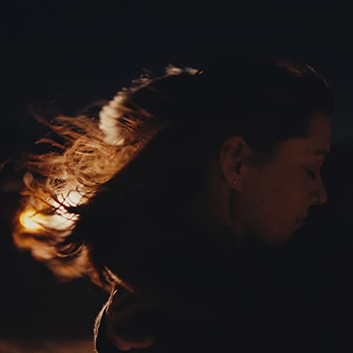 Close-up profile of a woman with windswept hair, illuminated by light.