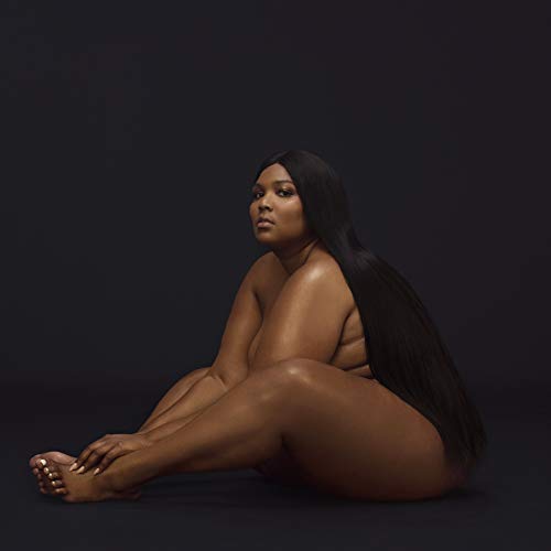 Lizzo with long dark hair sits against a plain black background.