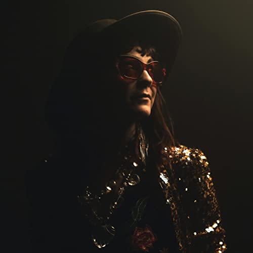 Carter Sampson in a hat and red sunglasses, wearing a gold jacket.