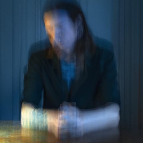 Blurred image of a person in a dark jacket, looking down.