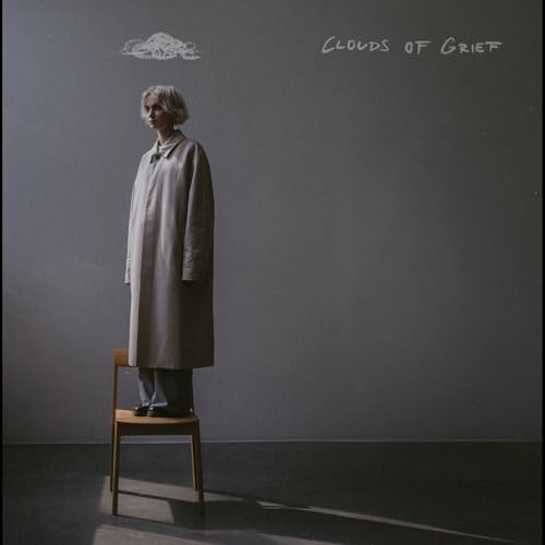Album cover: woman in coat sitting on chair, grey background.