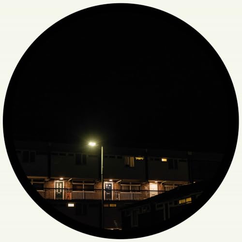 Dark circular image of a building at night under a streetlamp.