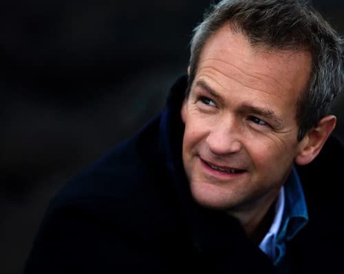 Close-up of a smiling man with short grey hair and a dark coat.