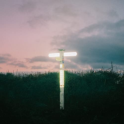 Road sign with faded stickers against a dusky pink and grey sky.