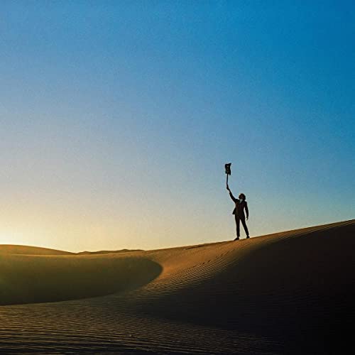 Silhouette of a person raising an object on a sand dune.