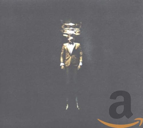 Man in suit with a crown-like object on his head, dark background.