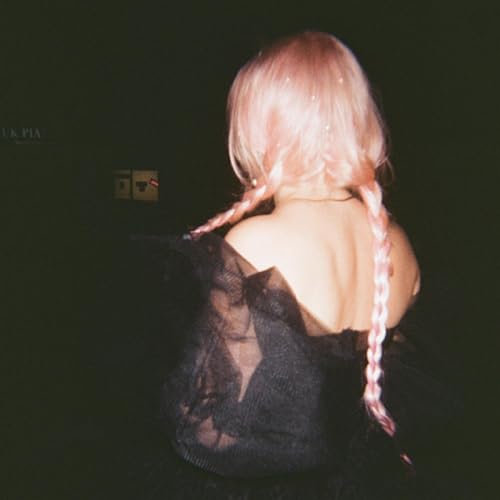 Woman with long pink braided hair, seen from behind in low light.